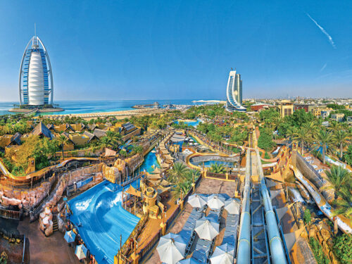 Aerial view of a large water park with winding slides, a wave pool, palm trees, and sun umbrellas showcases the ultimate getaway, offering three tiers of ROI for fun, relaxation, and adventure under a bright seaside sky.