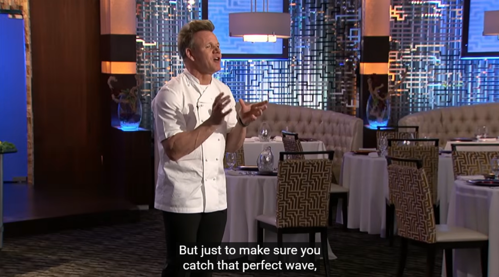 A chef in a white coat stands in a modern restaurant, gesturing with both hands. The subtitle reads, But just to make sure you catch that perfect FlowSurf wave, and tables are set in the background.