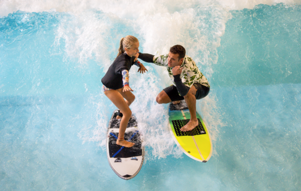 A man and a young girl surfing together on a FlowSurf wave machine.